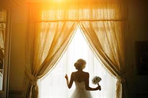 schöne Braut in einem Hochzeitskleid, am Fenster. foto