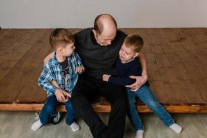 Papa sitzt mit zwei Söhnen auf dem Boden und umarmt sie. herzliche beziehung vater und söhne foto