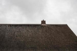 Antikes Dach aus natürlichen Materialien mit Schornstein vor bewölktem Himmel. foto