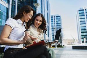 Zwei Geschäftsfrauen, die ein digitales Tablet verwenden, während sie eine Kaffeepause im Freien haben foto