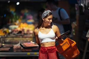 junge Frau wählt Fleisch in einem Lebensmittelgeschäft foto