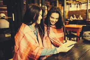 zwei Mädchen sitzen und hören Musik mit einem Smartphone foto