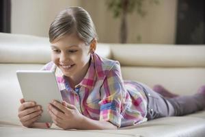 lächelndes Mädchen mit Tablet-PC beim Liegen auf dem Sofa