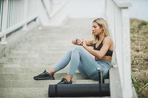 Frau, die auf Smartwatch schaut, während sie auf der Treppe sitzt, bevor sie im Freien trainiert foto