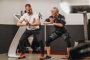 ältere frau, die ems-training mit trainer im fitnessstudio macht foto