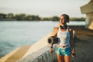 Frau mit aufgerollter Gymnastikmatte und Wasserflasche foto