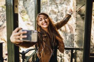 Frau, die ein Selfie per Smartphone macht, während sie mit einem Retro-Zug fährt foto