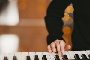 Eine Kinderhand spielt auf dem Digitalpiano vor dem Hintergrund einer Weihnachtsgirlande. Das Kind spielt den Synthesizer. musikalisches Hobby des Kindes. Der kreative Prozess zu Hause. foto