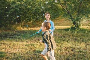 Jungs spielen mit Seifenblasen in einem Sommerpark im Grünen. Glückliche Kinder fangen Seifenblasen. foto