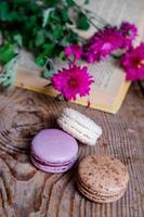 Macarons Hintergrund rote Blumen und Bücher, auf einem Holztisch. vertikaler Rahmen. Ästhetik mit Makronen und Blumen. schöne Kuchen auf einem Holztisch. morgens französisches frühstück. foto