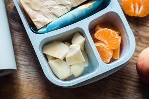 Schuljungenbrotdose mit Thermoskanne auf Holzhintergrund. Apfel, Mandarine, Sandwich in Brotdose und Wasserflasche foto