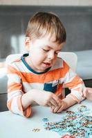 Junge in einem orangefarbenen T-Shirt sammelt ein Puzzle auf dem Tisch. Zeit ohne Gadgets. Brettspiele für Kinder. der junge entwickelt feinmotorik und gehirn foto