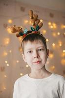 Porträt eines Jungen im Rentier-Weihnachtsgeweih auf dem Hintergrund einer orangefarbenen Girlande. Vorbereitung für die Weihnachtsfeier. Neujahrsmaskerade der Kinder foto