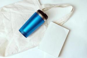 Segeltuchtasche, blaue Thermoskanne und Buch. Set für Spaziergänge im Park. Strand gesetzt. urlaubsvorbereitung.öko-stil foto