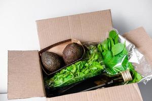 Box mit nützlichen Produkten. Avocado, Olivenöl, Spinat und Rucola in einer Schachtel. gesunde lieferung von lebensmitteln. gemüsesalat zutaten. foto