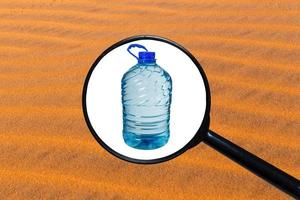 große Flasche Wasser isoliert auf weißem Hintergrund, Blick durch ein Vergrößerungsglas vor dem Hintergrund von Sand foto