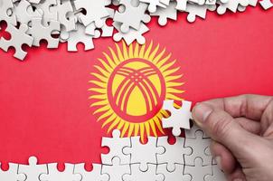 Die kirgisische Flagge ist auf einem Tisch abgebildet, auf dem die menschliche Hand ein weißes Puzzle faltet foto