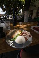 Nahaufnahme Scheiben von geräuchertem Speckfleisch mit Roggenvollkornschwarzbrot, Frühlingszwiebeln und Sauerrahm auf dem Tisch. foto