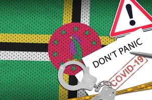 dominica-flagge und polizeihandschellen mit aufschrift keine panik auf weißem papier. Coronavirus- oder 2019-ncov-Viruskonzept foto