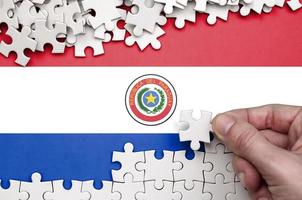 Die paraguayische Flagge ist auf einem Tisch abgebildet, auf dem die menschliche Hand ein weißes Puzzle faltet foto