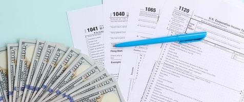 Steuerformulare liegen in der Nähe von Hundertdollarscheinen und blauem Stift auf hellblauem Hintergrund. Einkommensteuerrückerstattung foto