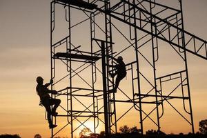 teamarbeit bauarbeiter installation gerüste im industriebau sonnenuntergang himmel hintergrund überstunden job silhouette. foto