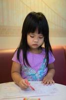 asiatisches Mädchen sitzt und färbt ein Bild in der Vorschule foto