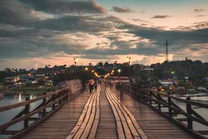 nicht erkennbare touristen, die abends in sangkhlaburi auf der mon-holzbrücke über den songkalia-fluss und das mon-dorf spazieren foto