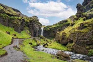 Kvernufoss-wasserfall, der an sonnigen sommertagen in island durch das grüne tal fließt foto