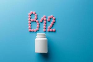 rosa pillen in form des buchstabens b12 auf blauem hintergrund, verschüttet aus einer weißen dose. foto