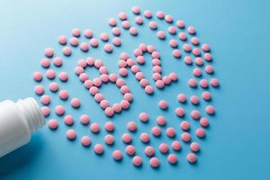 Rosafarbene Tabletten in Form von Vitamin B12 im Herzen auf blauem Hintergrund, verschüttet aus einer weißen Dose mit geringem Kontrast foto