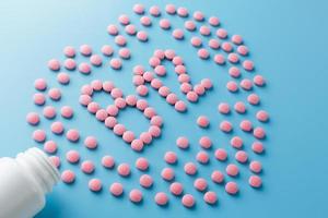 Rosafarbene Tabletten in Form von b12 im Herzen auf blauem Hintergrund, verschüttet aus einer weißen Dose. foto