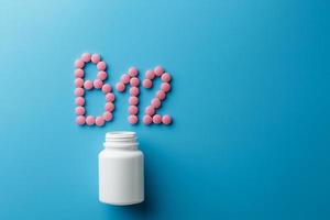 rosa pillen in form des buchstabens b12 auf blauem hintergrund, verschüttet aus einer weißen dose. foto