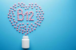 Rosafarbene Tabletten in Form von Vitamin B12 im Herzen auf blauem Hintergrund, verschüttet aus einer weißen Dose mit geringem Kontrast foto