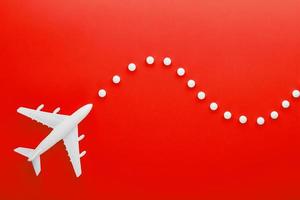 Weißes Passagierflugzeug mit Flugbahnpunkten, wie auf einer Streckenkarte, isoliert mit rotem Hintergrund. foto