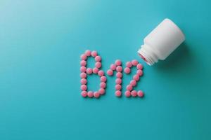rosa pillen in form des buchstabens b12 auf blauem hintergrund, verschüttet aus einer weißen dose, geringer kontrast foto