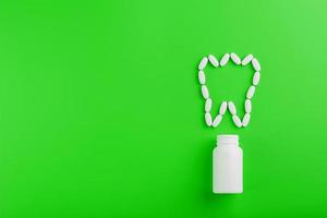 Kalziumvitamin in Form eines Zahns, der aus einem weißen Glas auf grünem Hintergrund verschüttet wurde. foto