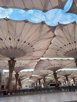 medina, saudi-arabien, 2022 - regenschirmkonstruktion auf dem platz von al-masjid an-nabawi oder der propheten-muhammed-moschee schützen die menschen tagsüber vor der sonne und arbeiten nachts als lichter foto