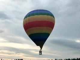 großer, bunter, heller, runder, regenbogenfarbener, gestreifter, fliegender Ballon mit einem Korb gegen den Himmel am Abend foto