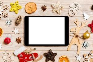 Draufsicht des Tablets auf hölzernem Hintergrund des Feiertags. neujahrsdekorationen und spielzeug. Weihnachtskonzept foto