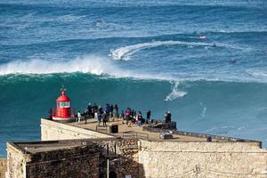 nazare, portugal - 7. november 2022 surfer reitet auf einer riesigen großen welle in der nähe des forts von sao miguel arcanjo leuchtturm in nazare, portugal. größten wellen der welt. touristisches Ziel zum Surfen