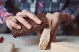 Tischlerhände polieren Holzbohlen mit Sandpapier. foto