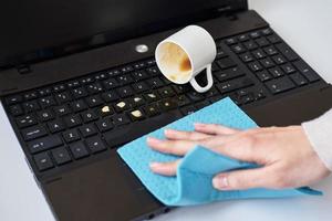 Hand reinigt verschütteten Kaffee auf der Laptop-Tastatur mit einem Lappen foto