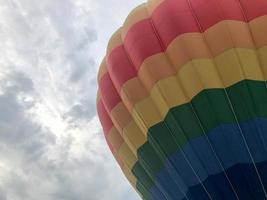 großer, bunter, heller, runder, regenbogenfarbener, gestreifter, fliegender Ballon mit einem Korb gegen den Himmel am Abend foto