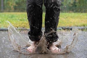 barfüßige weibliche Füße springen in eine Pfütze, nach Regen sprühen Spritzer in verschiedene Richtungen. Foto in Bewegung, Unschärfe. Unterhaltung, Lebensstil.