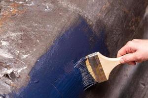 Hand malt eine gusseiserne, alte Badewanne mit schwarzer Farbe mit einem Pinsel. Hausrenovierung. Nahansicht. foto