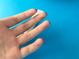 auf einer blauen matten Hintergrundhand. Die Finger des Mädchens mit leuchtend roter Maniküre auf dem medizinischen Tisch. Planen Sie einen Fingerstick-Test zur Bestimmung von Antikörpern foto