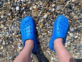 Männerbeine, Füße in blauen Gummipantoffeln vor dem Hintergrund von Kieselsteinen und Sand bei einem Urlaub am Strand in einem warmen tropischen östlichen Paradies Country Southern Resort foto