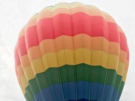 großer, bunter, heller, runder, regenbogenfarbener, gestreifter, fliegender Ballon mit einem Korb gegen den Himmel am Abend foto