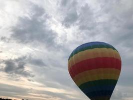 großer, bunter, heller, runder, regenbogenfarbener, gestreifter, fliegender Ballon mit einem Korb gegen den Himmel am Abend foto